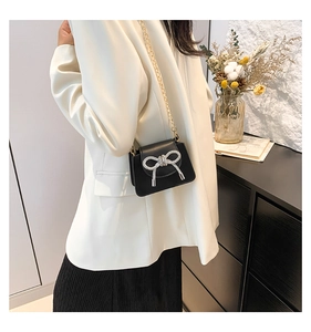 Detail of elegant black crossbody bag with silver rhinestone bow and gold chain strap