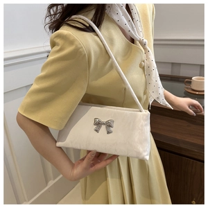 Sac bandoulière beige chic avec boucle nœud argentée porté sur une robe blazer