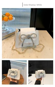 Detail of elegant white mini bag featuring a sparkling rhinestone bow and gold chain strap