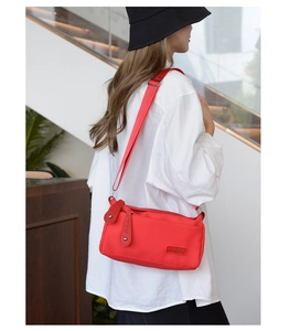 Detailed side view of the bright red waterproof nylon crossbody bag on a female model