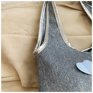 Detail of blue denim shoulder bag with silver trim and heart-shaped decorative patch