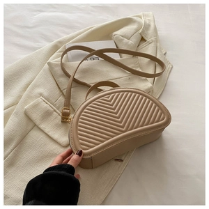 Dettaglio borsa a mezzaluna trapuntata beige con cuciture a V e texture in pelle liscia