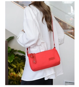 Detail of red nylon crossbody bag showing the sleek strap and square label on a model