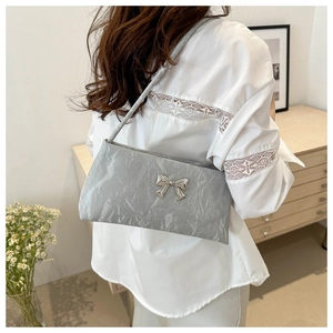 Détail du sac à main plissé argenté avec nœud papillon porté à l'épaule en style de vie