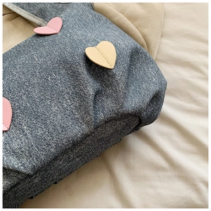 Close-up of denim tote bag featuring pink heart patches and refined stitching details