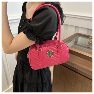 Detail of fuchsia quilted shoulder bag with V-stitch patterns and gold medal emblem