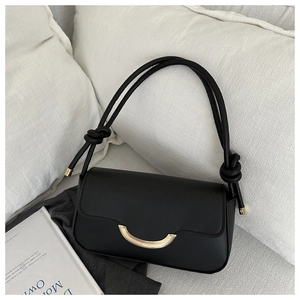 Détail d'un sac à bandoulière noir minimaliste montrant la boucle dorée et le cuir lisse