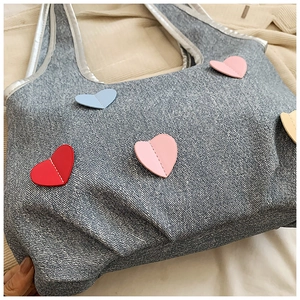 Detailed close-up of gray denim tote bag featuring colorful heart patches and stitching