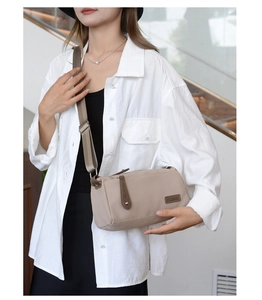 Detail of a beige nylon crossbody bag with brown leather accents on a model