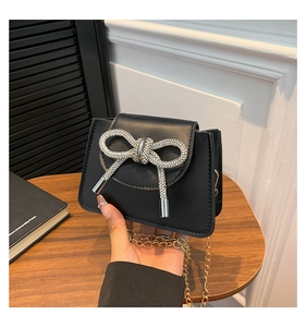 Detail of a mini black crossbody bag featuring a sparkling rhinestone bow and gold chain
