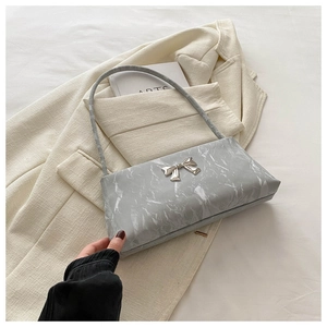 Détail de la boucle noeud argentée sur un sac gris marbré posé sur un blazer beige