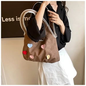 Detail of a brown canvas tote bag featuring colorful heart patches and silver trim handles