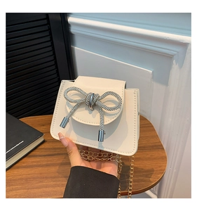Detail of a creamy white mini chain bag featuring a luxury sparkling rhinestone bow accent