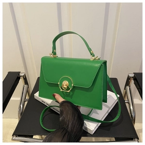 Detail of green leather square bag with gold circular buckle on a minimalist background