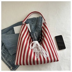 Close-up of red striped canvas bucket bag with lace bow on a textured fabric background