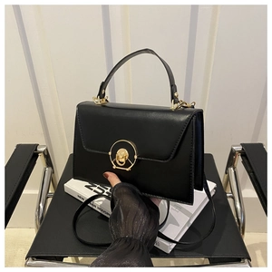 Detail of black crossbody bag featuring gold round buckle and elegant envelope flap design