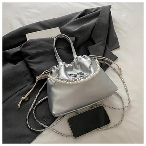 Détail du sac à cordon argenté métallisé avec chaîne en perles et boucle à nœud sur costume gris