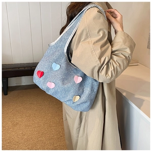 Detail of denim tote bag with colorful heart patches and silver trim on shoulder