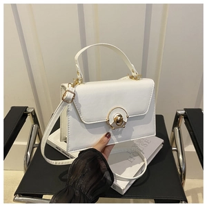 Detail of white leather crossbody bag featuring a golden circular clasp and elegant top handle