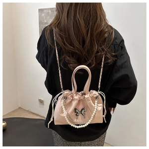 Sac seau rose à cordon avec chaîne perlée et boucle papillon porté par un modèle