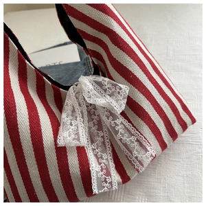 Detail of red striped canvas bag featuring a large white lace bow and herringbone texture
