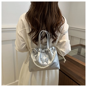 Détail d'un sac à main argenté plissé avec ornement papillon et chaîne en perles