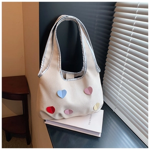 Close-up of heart patches on cream canvas tote bag with metallic silver trim detail