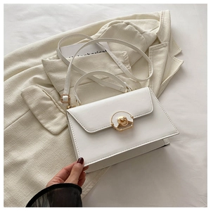 Detail of off-white leather handbag with gold circular lock on beige blazer background
