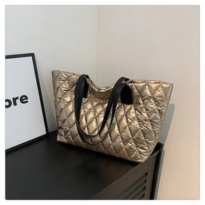 Close-up of golden quilted tote bag with black straps and metallic finish texture