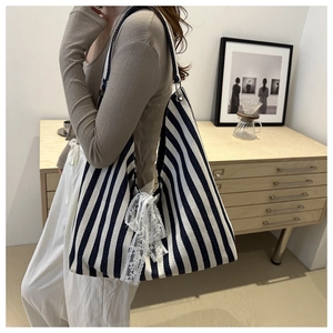 Detail view of striped canvas tote bag featuring a white lace bow on the side in a lifestyle setting