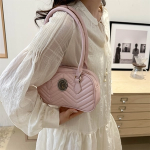 Quilted light pink shoulder bag with vintage metal emblem on white dress model