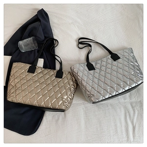 Quilted tote bags in metallic gold and silver with black handles on a white fabric surface