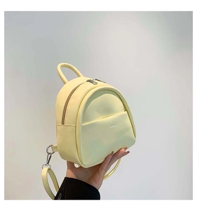 Détail d'un mini sac à dos jaune en cuir synthétique texturé tenu par une main