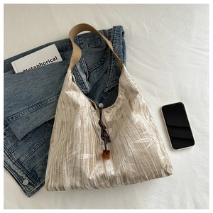 Détail du sac cabas plissé beige avec motif de feuilles, sangle brune et perle