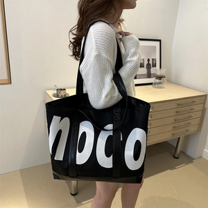 Grand sac cabas noir avec imprimé noco blanc porté par un mannequin dans un décor sobre