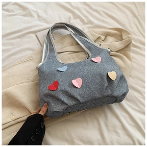 Detail of denim tote bag featuring colorful heart patches and silver metallic trim edges