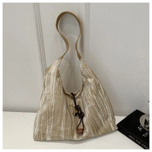 Détail du sac cabas plissé champagne avec texture luxueuse et décor de pendentif ambre