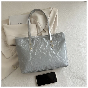 Detail of silver crinkled metallic tote bag with golden rivets and slim shoulder straps