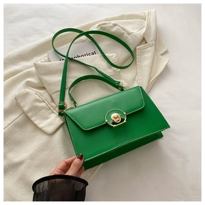 Detail of green square handbag with gold circular metal clasp and adjustable shoulder strap