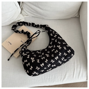 Detail of black canvas hobo bag featuring white bow prints and ruched shoulder strap design
