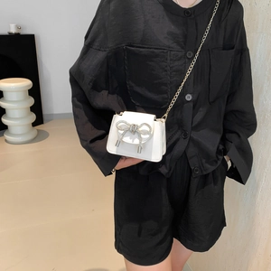 Chic white mini crossbody bag with diamond bow detail and gold chain strap on model