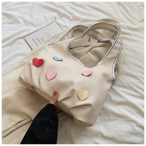 Detail of off-white canvas tote bag featuring colorful heart patches on a soft fabric surface