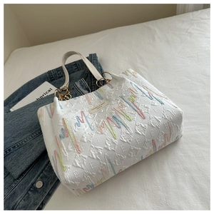 Detail view of white quilted tote bag featuring colorful embroidery and metal chain strap