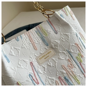 Detail of white textured tote bag with colorful embroidery and gold metal chain strap