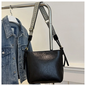 Detail of black leather bucket bag with vintage geometric jacquard woven strap