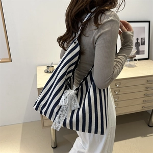 Striped canvas tote bag with white lace bow detail shown in a casual lifestyle setting