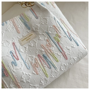 Detail of white tote bag featuring colorful wavy embroidery and a leather brand tag