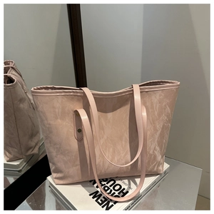 Detail of a large tote bag with pink marble texture and leather handles on a book