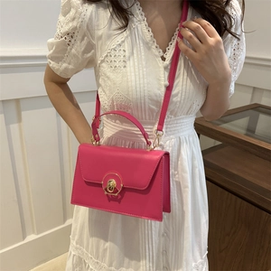 Sac à main carré magenta avec fermoir doré porté par un modèle en robe dentelle