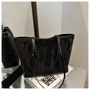 Detail of black tote bag featuring crinkled glossy texture and leather shoulder straps